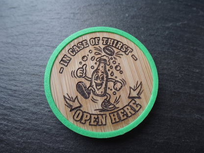 A round wood opener with a green border, featuring a cartoon bottle character and the text 'IN CASE OF THIRST OPEN HERE' on a dark slate background.