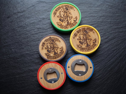 Five round bottle opener coasters arranged on a dark slate surface. Each coaster has a wood-grain center with a metal bottle opener cutout, surrounded by a different rim color: green, grey, yellow, red, and blue.