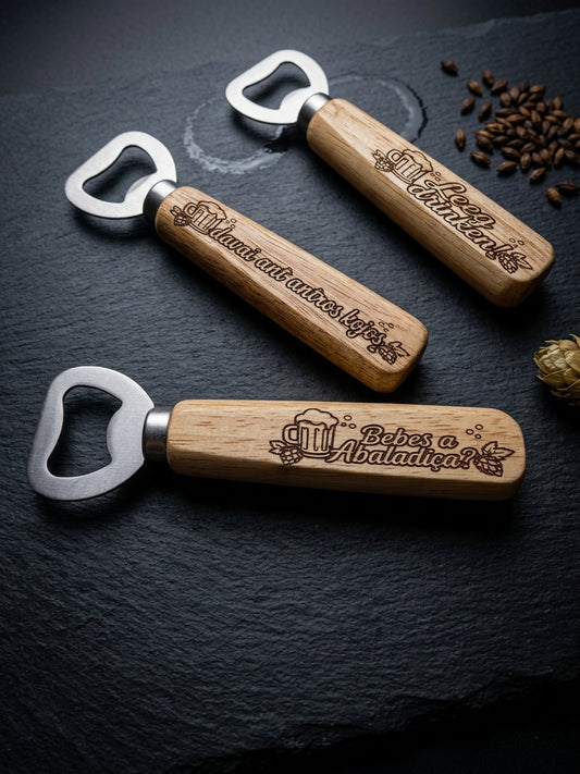 Three personalized wooden bottle openers with silver metal keys are arranged diagonally on a dark slate surface with coffee beans