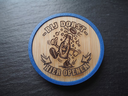 A round wooden coaster with a blue outer rim, featuring a laser-engraved cartoon beer bottle character and the Dutch text '-BIJ DORST- HIER OPENEN' on a dark slate background.