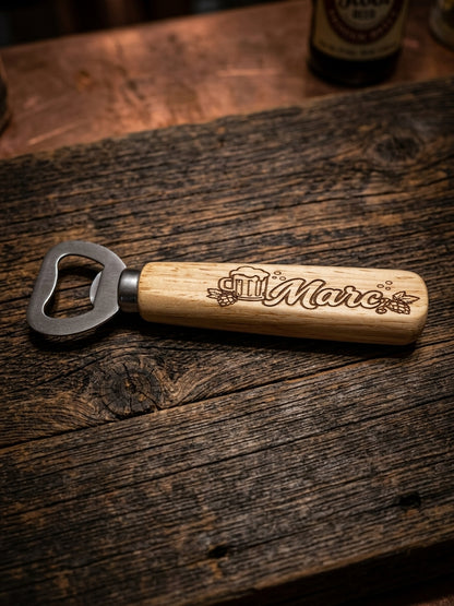 A wooden handled bottle opener engraved with 'Marc' and a beer mug, resting on a rustic dark wood tabletop.