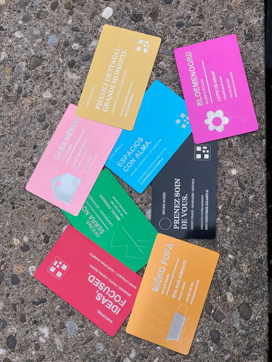 Eight colorful business cards with custom text are arranged in a circle on a textured gray concrete surface. The cards feature various vibrant colors including pink, blue, green, black, orange, and gold, each with a small white logo and placeholder company names.