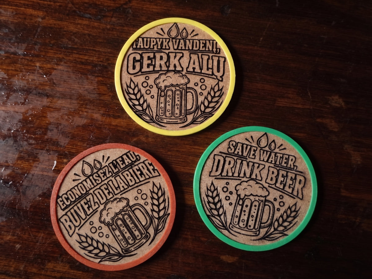 Three round wooden beer coasters with engraved beer mug designs and Lithuanian, French and English phrases, displayed on a dark wooden tabletop. One coaster has a yellow rim, one has an brown rim, and one has a green rim.