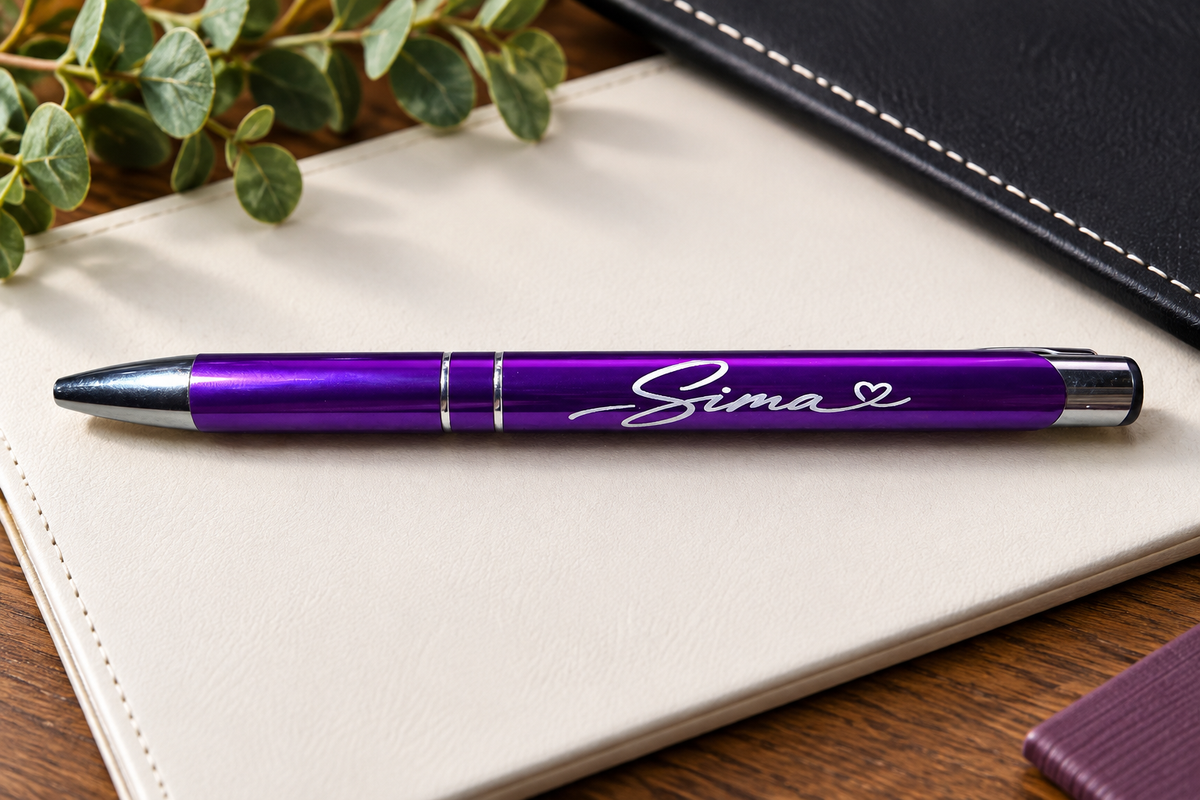A metallic purple ballpoint pen with the engraved name 'Sima' written in white script, resting on a cream-colored notebook. 