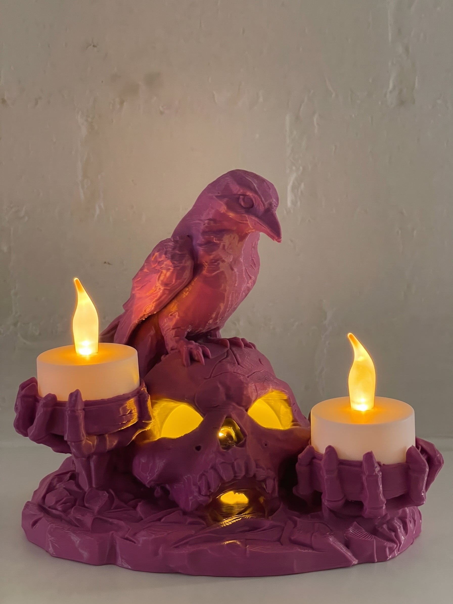 Pink Halloween skull and raven candle holder with three warm glowing LED candles.