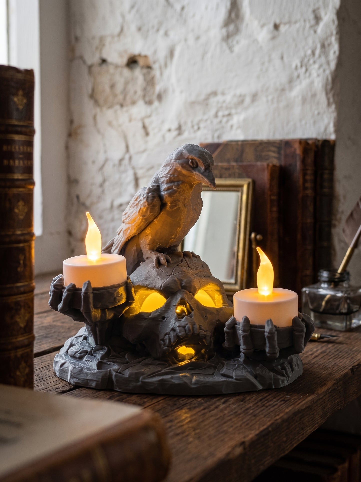 A gothic-style skull candle holder with a raven perched on top, holding two lit white pillar candles, displayed on a rustic wooden table in a vintage room setting.