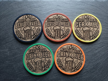 Five round beer-themed coasters arranged on a dark slate surface. Each coaster has a tan center with a beer mug and wheat illustration, surrounded by a different border color: black, brown, yellow, green, and orange.