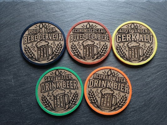 Five round beer-themed coasters arranged on a dark slate surface. Each coaster has a tan center with a beer mug and wheat illustration, surrounded by a different border color: black, brown, yellow, green, and orange.
