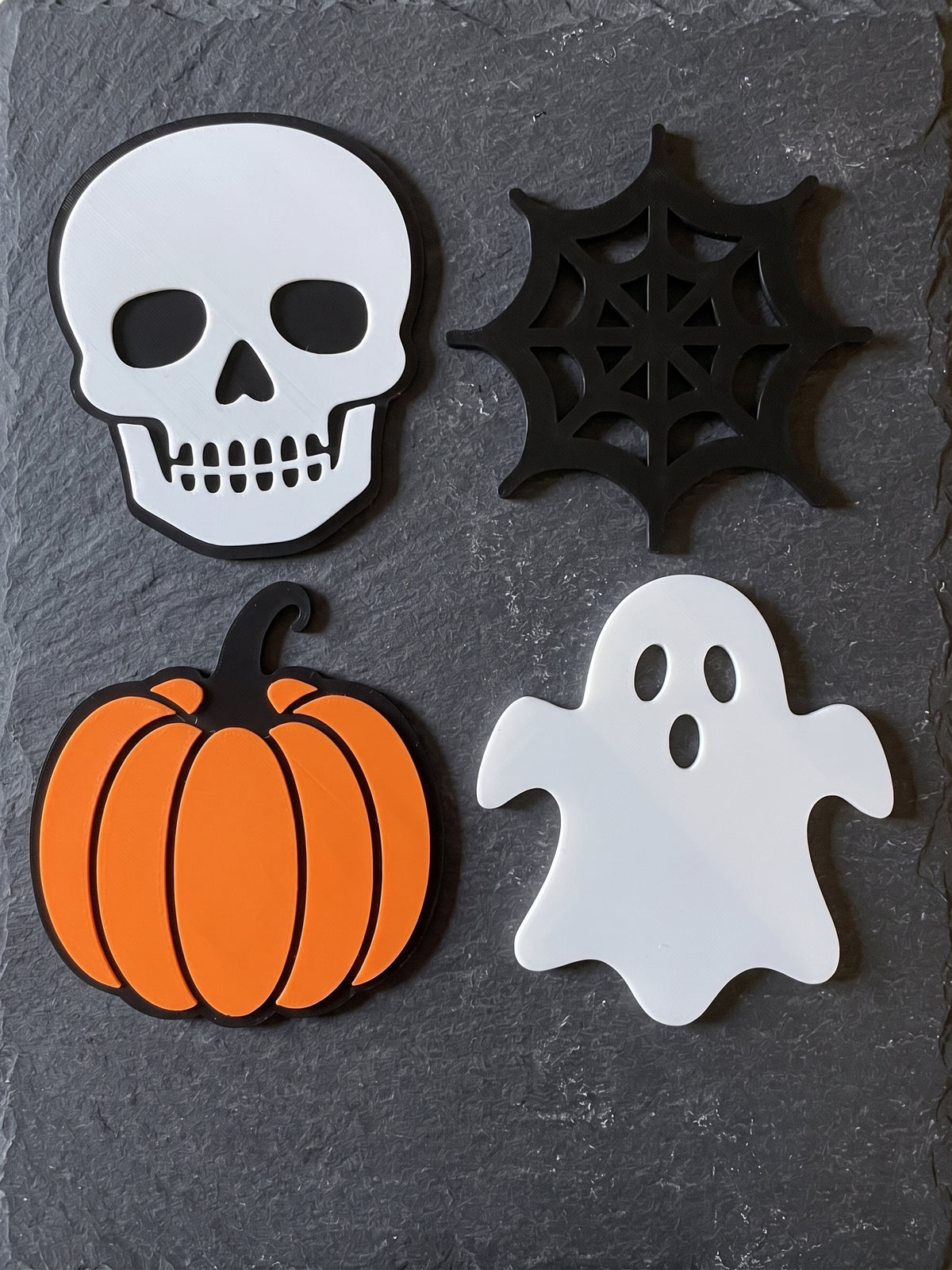 Four Halloween coasters showing skull, spider web, pumpkin and ghost on a surface.