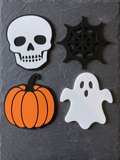 Four Halloween coasters showing skull, spider web, pumpkin and ghost on a surface.
